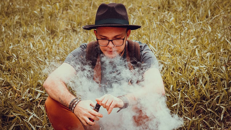 Jeune homme assis qui tient une cigarette électronique